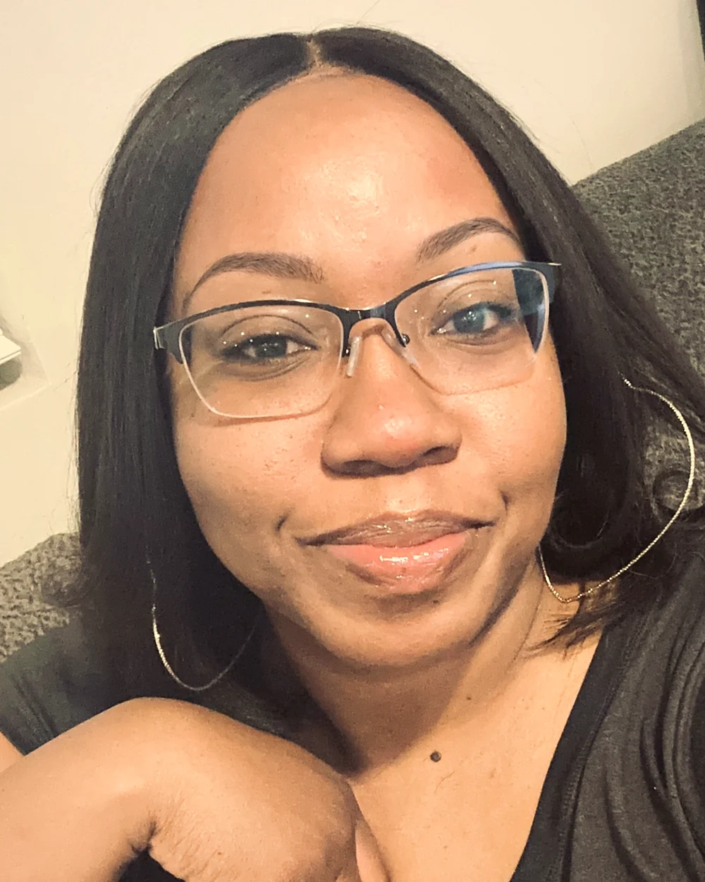 Amber Cotton, smiling, in glasses and gold hoop earrings.